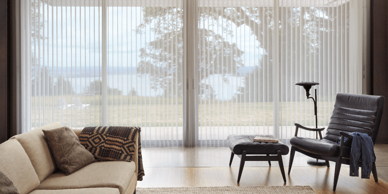 Living room with a sofa and accent chair with ottoman set in front of large sliding patio doors with Luminette blinds.